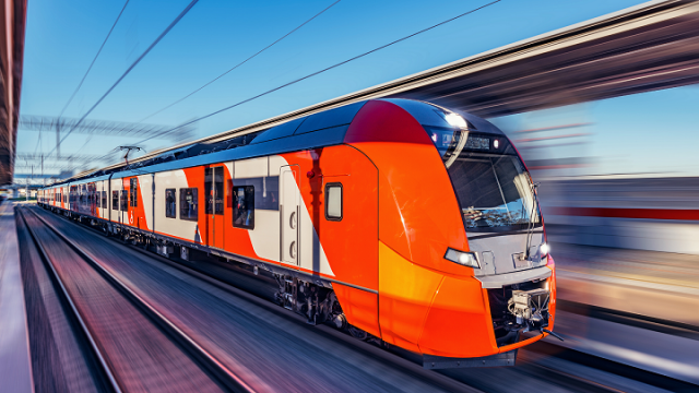 A red train is running on the tracks, the background is blurred because of the high speed.