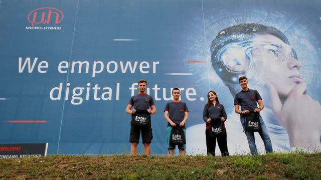 Gruppenbild der neuen Azubis vor dem Micro-Hybrid Werbeplakat