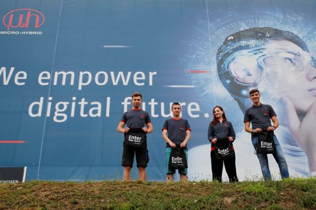 Gruppenbild der neuen Azubis vor dem Micro-Hybrid Werbeplakat