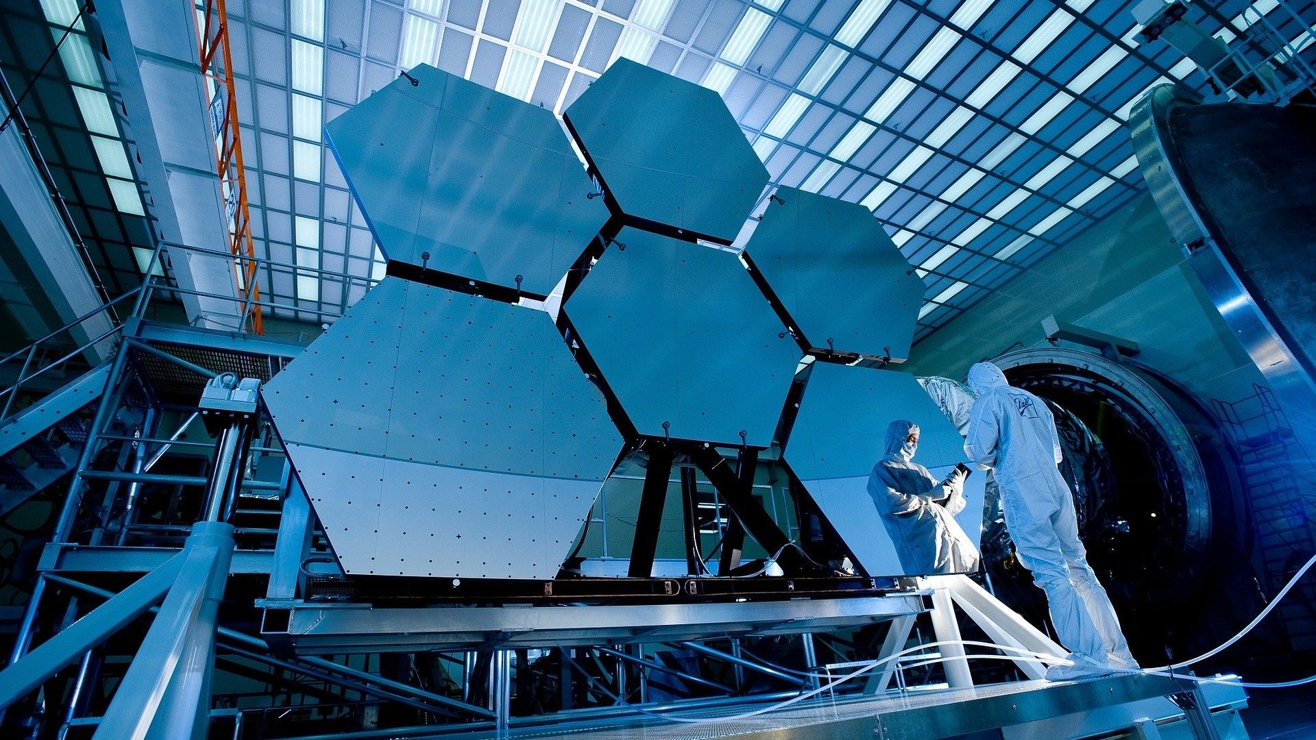 Men stand infront of a large telescope mirror and look at a tablet