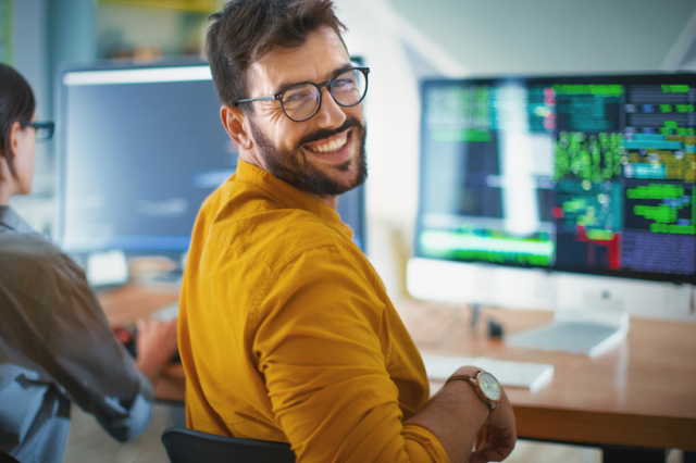 Man sits at a PC and looks over his shoulder to the viewer