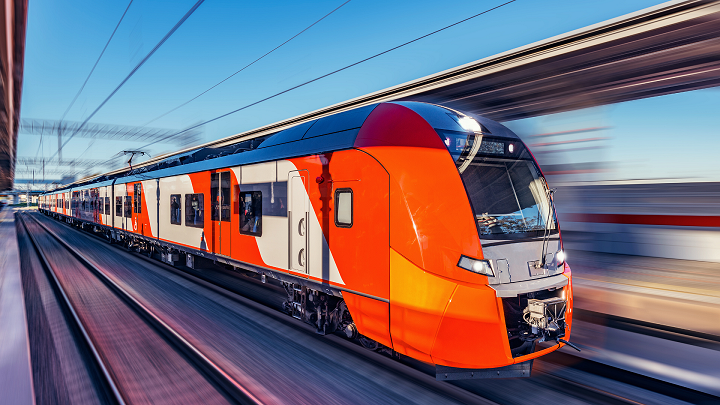 Ein roter Zug fährt auf den Gleisen, der Hintergrund ist wegen der hohen Geschwindigkeit verschwommen.