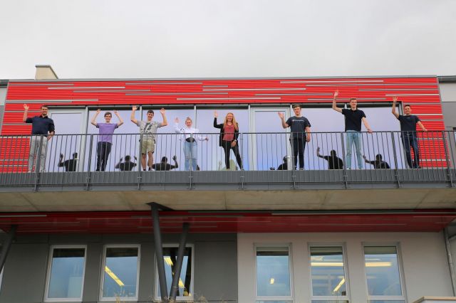 Neue Studierende und Auszubildende stehen auf dem Balkon des Micro-Hybrid Firmengebäudes und winken