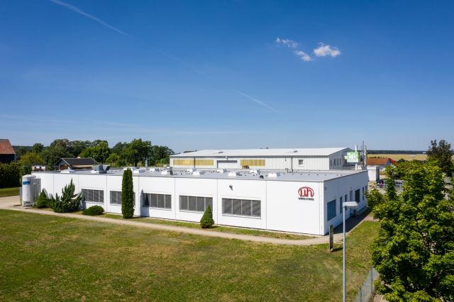 Das weiße Niederlassungsgebäude in Münchenbernsdorf mit Micro-Hybrid-Logo an der Hauswand.