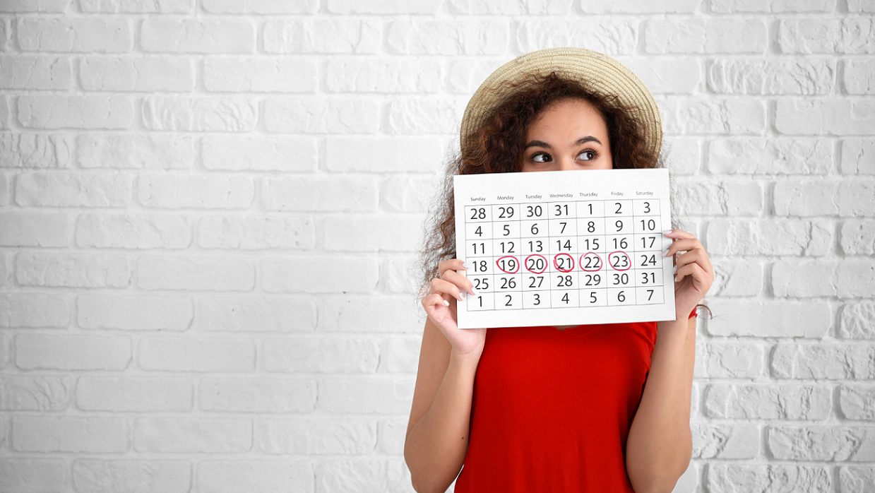 Frau mit Monatskalender in der Hand vor weißer Wand