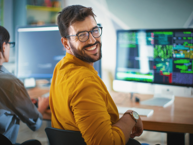 Man sits at a PC and looks over his shoulder to the viewer