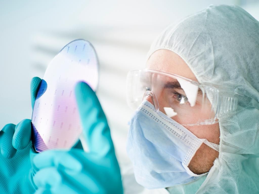 Ein technischer Mitarbeiter in Schutzkleidung für einen Reinraum prüft optisch einen Siliziumwafer