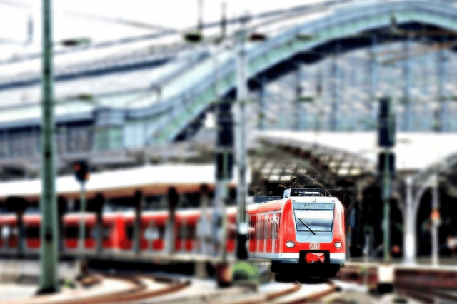 Ein roter Zug der Firma Deutsche Bahn fährt aus einem großen überdachten Bahnhof heraus