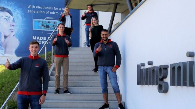 Four trainees and two employees stand on a staircase in front of the company building of Micro-Hybrid