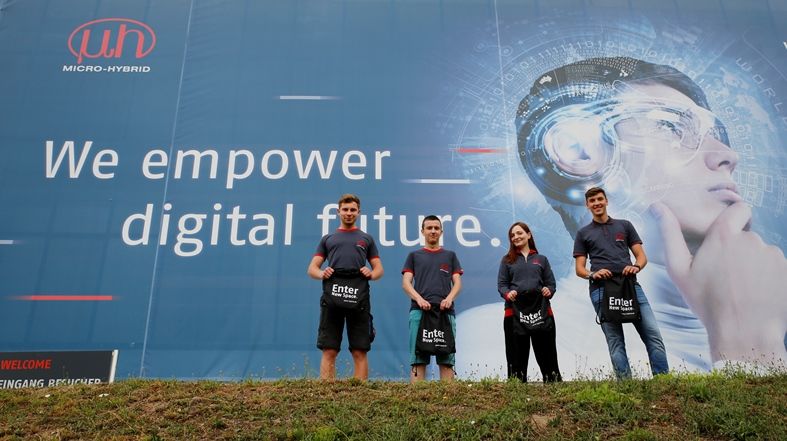 Gruppenbild der neuen Azubis vor dem Micro-Hybrid Werbeplakat